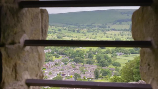 Wide high angle tilting shot of Castleton village through the metal grill window inside the historic Peveril Castle, Peak District, Derbyshire, UK