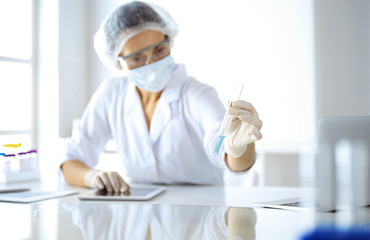 Professional female scientist in protective eyeglasses researching tube with reagents in...