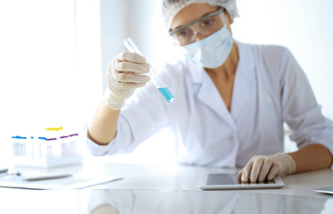 Professional female scientist in protective eyeglasses researching tube with reagents in laboratory. Concepts of medicine and research