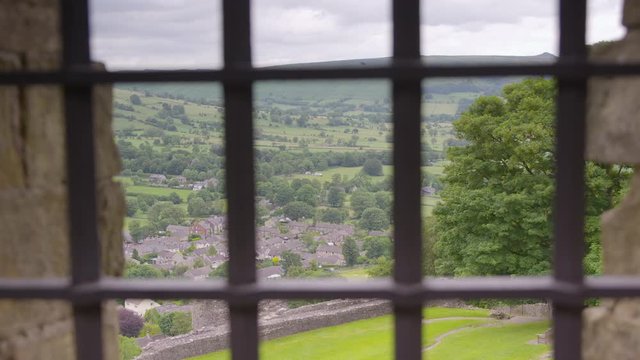 Wide high angle panoramic still view from metal grill window of Peveril Castle of Castleton valley village and landscape, heritage park, Peak District, Derbyshire