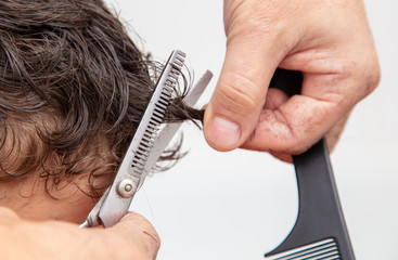 Hairdresser cuts the hair of a boy with scissors