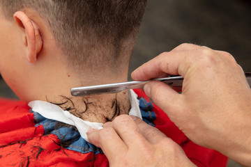 The hairdresser cuts the boy's hair with a razor