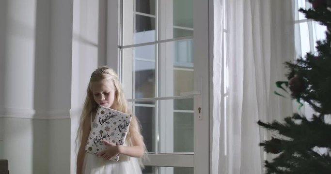 Cute Caucasian girl with blond hair waving to Santa, man leaving, child sitting down with Christmas present. Childhood, miracle, Christmas. Cinema 4k ProRes HQ.
