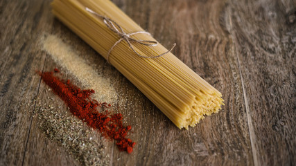 Uncooked spaghetti and spices (dry garlic, dry tomato powder, oregano) on a wooden background.