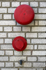 red fire alarm bell and hose connector on white brick wall