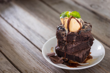 Chocolate brownies stacks and vanila ice cream on top, wooden background