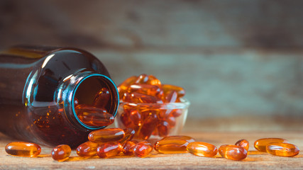 Fish oil pills in a glass bottle on wooden table and texture, vitamin D and omega 3 source from...