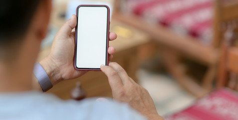 Close-up view of young man holding smartphone in comfortable office room
