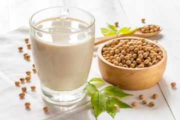 Soy or soya milk in a glass with soybeans in wooden bowl background