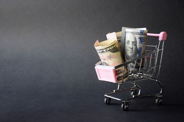 Shopping trolley with dollars banknotes on a black background. Dollars bill note with copy space in selective focuse. Money growth concept.