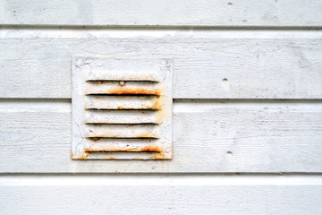 Old rusty ventilation grill in a dirty white wooden wall.