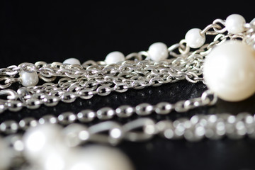 Modern necklace made of silver chains and white beads close-up on a dark surface. Fashion background