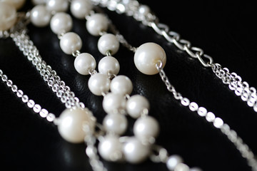 Modern necklace made of silver chains and white beads close-up on a dark surface. Fashion background