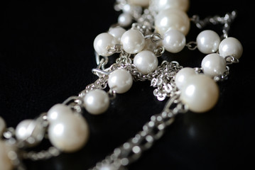 Modern necklace made of silver chains and white beads close-up on a dark surface. Fashion background