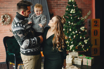 Fototapeta premium Beautiful family sitting near Christmas tree. Cute mother in a green dress. Little boy with handsome father