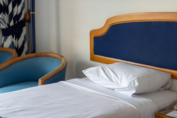 Hotel room with dark blue dÃ©cor, fitted bed, white-blue striped curtains and light blue lounge chairs.