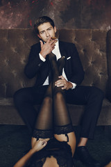 Elegant man in a black suit. Couple at home. Hot woman in a black underwear. Male with cigar