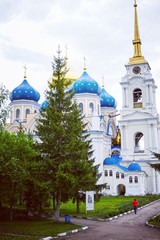 Fototapeta na wymiar Orthodox Church with blue and gold domes on a cloudy summer day, in front of the Church grow large fir trees