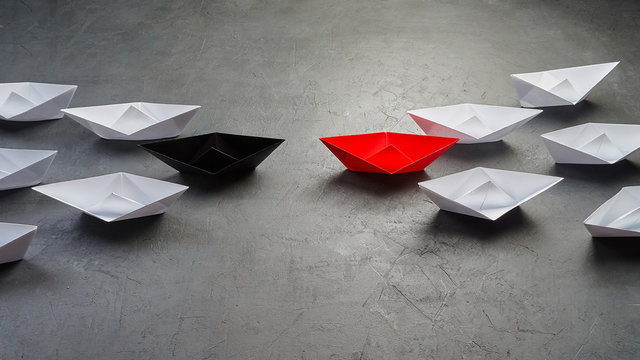  Leading In The Direction Of The White Ships Goes To Meet The Red Paper Boat Which Leads The White Ships On A Gray Concrete Background, Shows How The Meeting Of Two Businessmen On The Same Site