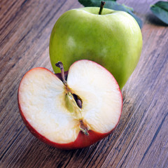 Green apple and sliced red apple on a wooden table