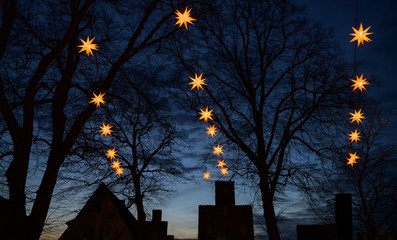Illuminated Herrnhuter Moravian Christmas stars hanging above the dark silhouettes of old house...