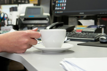 White tea cup with hand on computer desk in office