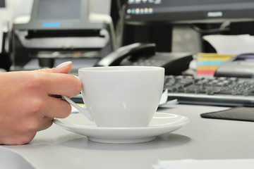 White tea cup with hand on computer desk in office