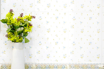 Yellow flowers in the white vase front of flowers pattern tile in the toilet.