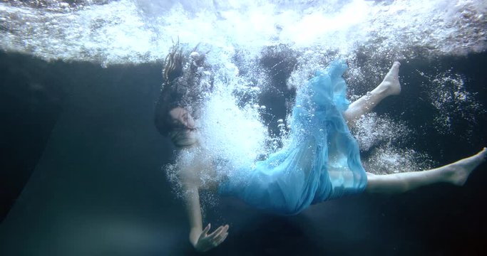 woman in blue dress falls down into water slow motion