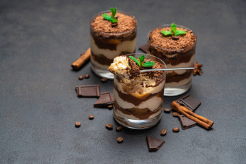 Classic tiramisu dessert in a glass cup and pieces of chocolate on dark concrete background
