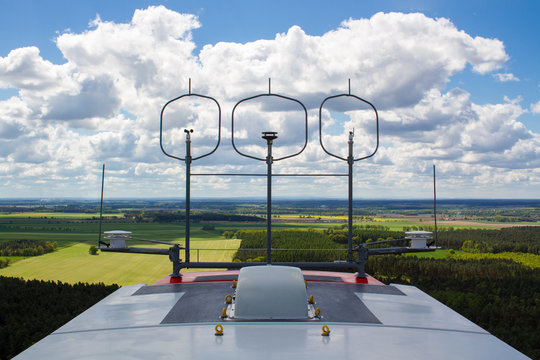Measurement devices (cup anemometer, ultrasonic anemometer, wind vane) and aviation lights on the nacelle roof of a wind turbine with fields and cloudy sky in the background
