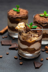 Classic tiramisu dessert in a glass cup and pieces of chocolate on dark concrete background