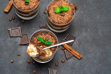 Classic tiramisu dessert in a glass cup and pieces of chocolate on dark concrete background