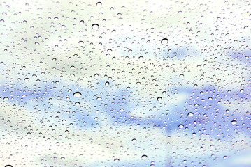 Closeup and crop rain drop on glass and blurry light blue background