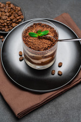 Classic tiramisu dessert in a glass cup and pieces of chocolate on dark concrete background