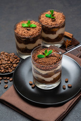 Classic tiramisu dessert in a glass cup and pieces of chocolate on dark concrete background