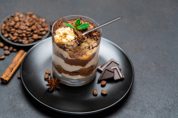 Classic tiramisu dessert in a glass cup and pieces of chocolate on dark concrete background