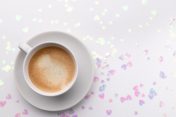 Holographic glitter confetti in heart shape and cup of coffee on white background