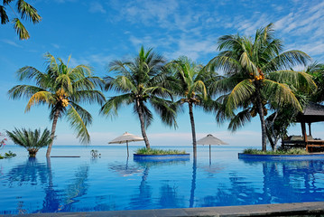 Luxury infinity swimming pool with blue water, umbrellas, palms and endless ocean view. Bali, Indonesia.