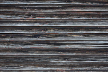 The texture of an aged wooden wall of planks without painting. Old wall made of curved dark planks