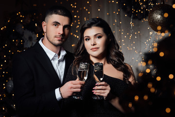 Loving couple, is stylishly dressed near a Christmas tree. Christmas time. Christmas mood. Loving couple celebrating New Year and Christmas with champagne. A bearded guy with a girl pose in a studio 