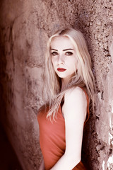 Fototapeta premium Blondes Mädchen/Frau post an der Wand mit einem roten Kleid