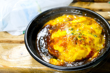 Omelet with cheese and sauce on rice in black take away bowl