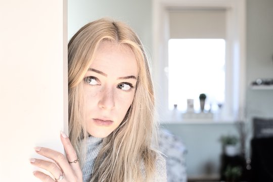 Blonde junge Frau schaut be&auml;ngstigend hinter der T&uuml;r