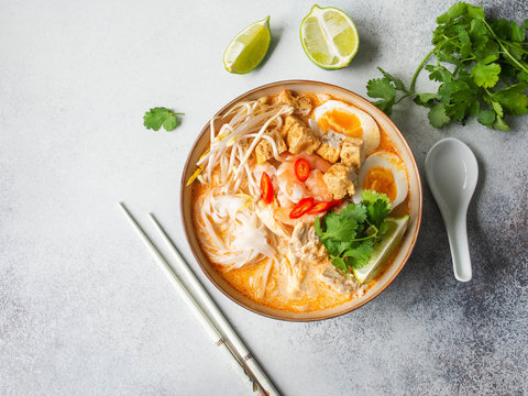Malaysian noodles laksa soup with chicken, prawn and tofu in a bowl on grey background