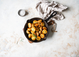 Black cast iron pan with fried roasted potato wedges with herbs on a light background.