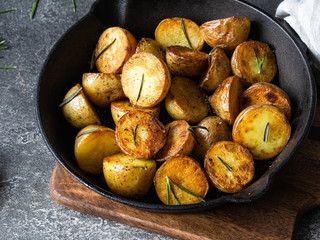 Black cast iron pan with fried roasted potato wedges with herbs on dark gray background