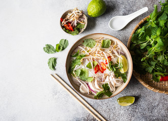 Traditional Vietnamese soup- pho ga in bowl with chicken and rice noodles, mint and cilantro, red onion, chili, bean sprouts and lime on grey background. Asian food. Copy space. Top view - obrazy, fototapety, plakaty