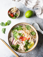 Traditional Vietnamese soup- pho ga in bowl with chicken and rice noodles, mint and cilantro, red onion, chili, bean sprouts and lime on grey background. Asian food. Copy space. Top view