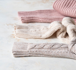 Fototapeta na wymiar Sleeves of three of warm different knitted woolen sweaters pastel shades beige textured background.